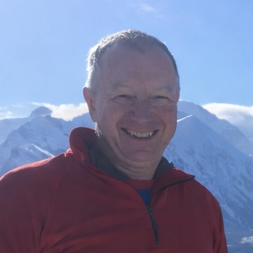Man in a red jacket standing in front of snow-capped mountains